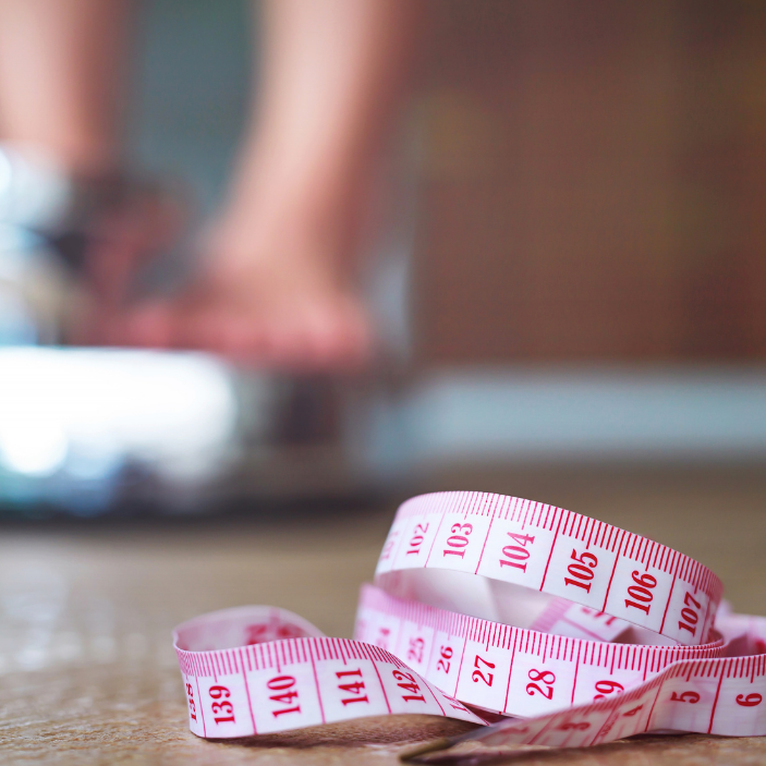Close-up of a measuring tape on a wooden surface with blurred feet in the background