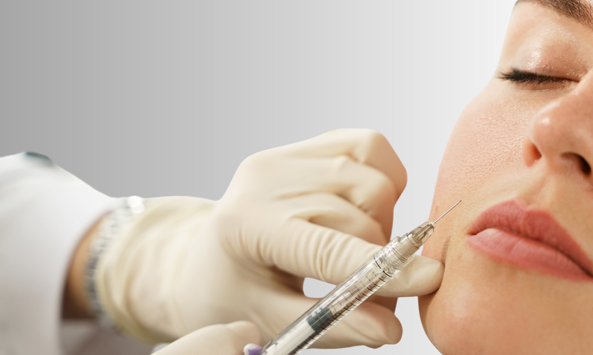 Person receiving a facial injection with a syringe held by a gloved hand.