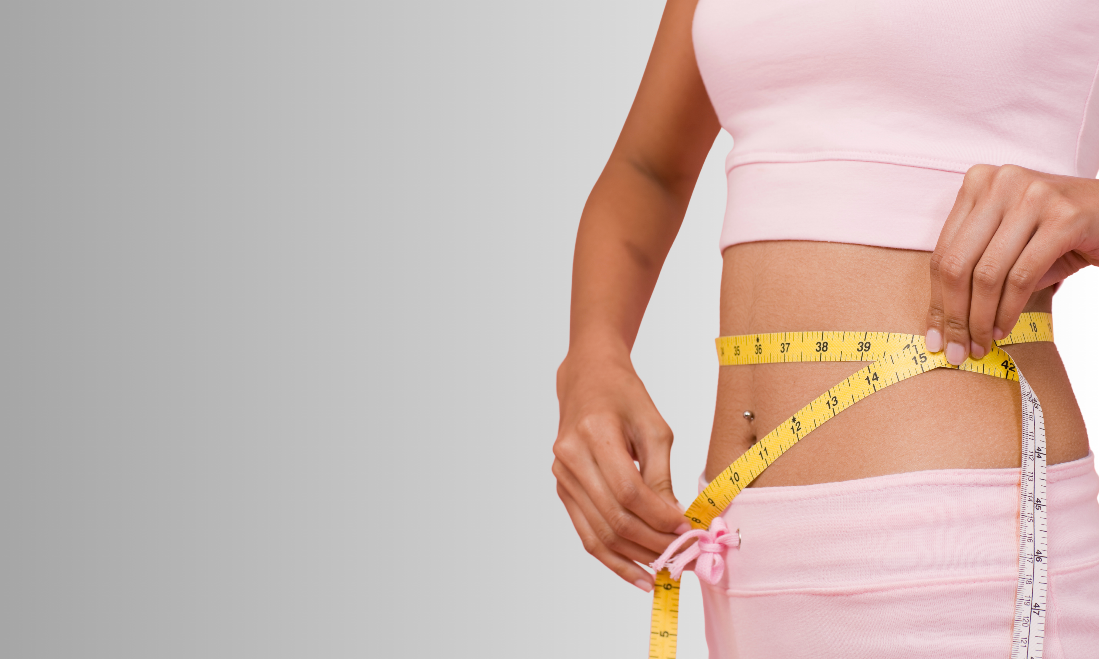 Person measuring waist with a tape measure on a plain background