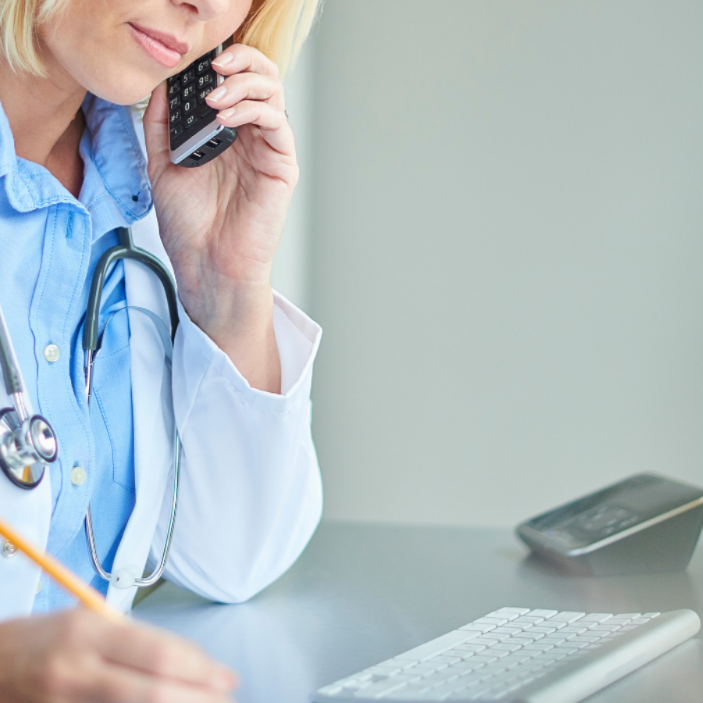 Doctor talking on a phone with a laptop and notebook in the background