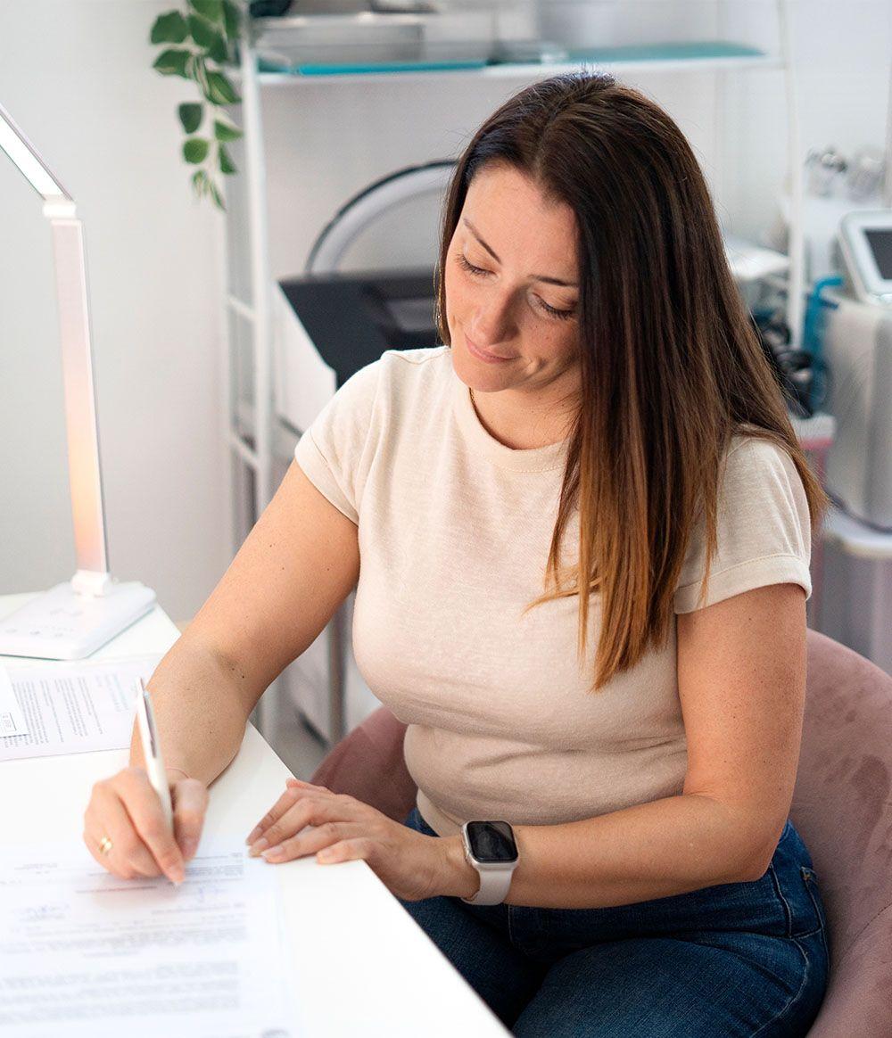Woman sitting at a desk in an office setting, writing on a piece of paper.