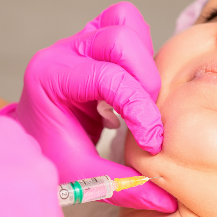 Person receiving a facial injection with pink gloves on a neutral background